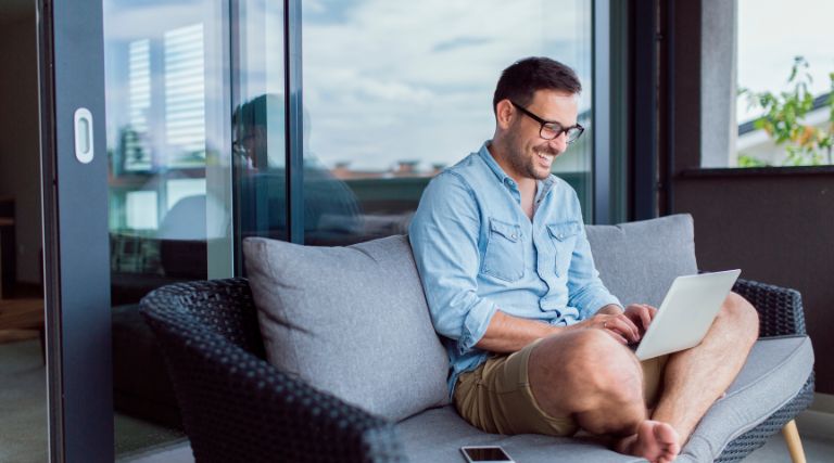 Man sitting on a couch with laptop. Learn the top 10 cybersecurity tips for remote working.